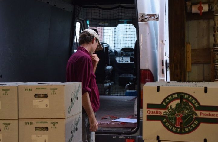 Chris looking at a clipboard in the back of their van with CSA boxes in the foreground