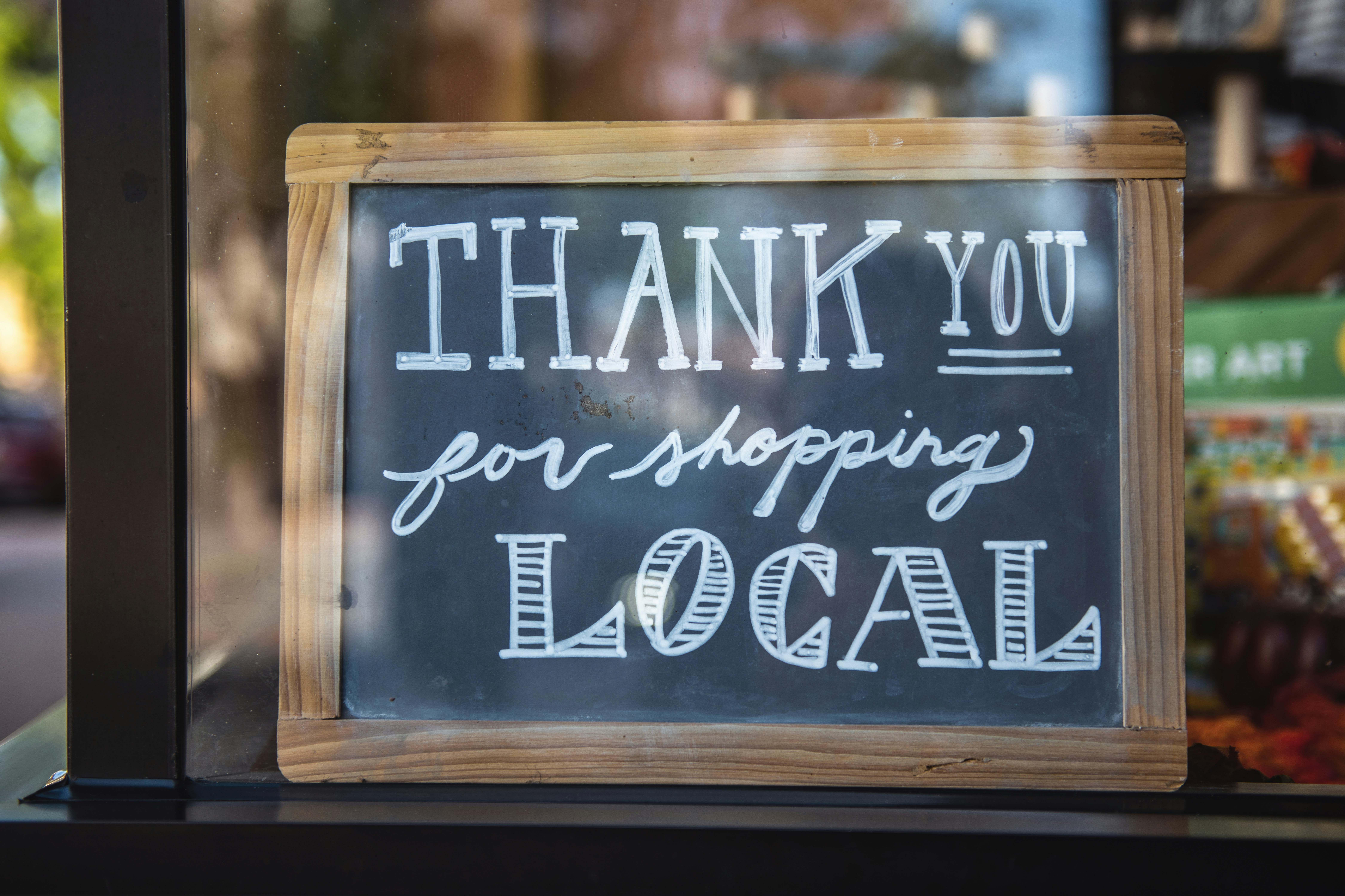 Small wooden framed blackboard that says "Thank you for shopping local" in white chalk.